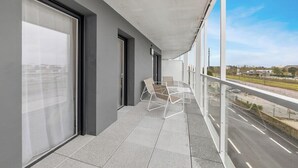 Un balcón con vista a una calle y edificios, una puerta de cristal y una silla.