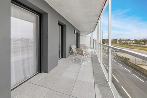 Ein Balkon mit Blick auf eine Straße und Gebäude, eine Glasdoor und ein Stuhl.