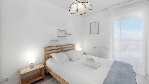 Un dormitorio moderno con una cama de madera, mesitas de noche, una lámpara colgante y vistas de la ciudad a través de un ventanal grande.
