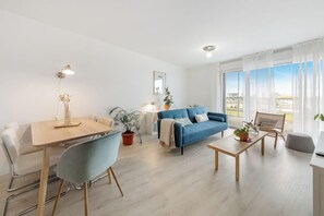 Een moderne woonkamer met een eettafel, blauwe bank en een groot raam met uitzicht.