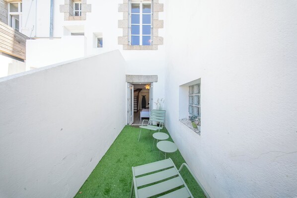 A narrow courtyard with artificial grass, a small seating area, and a door leading to an interior space. - La Rabine – Bel Appartement avec Terrasse Privée (Vannes)