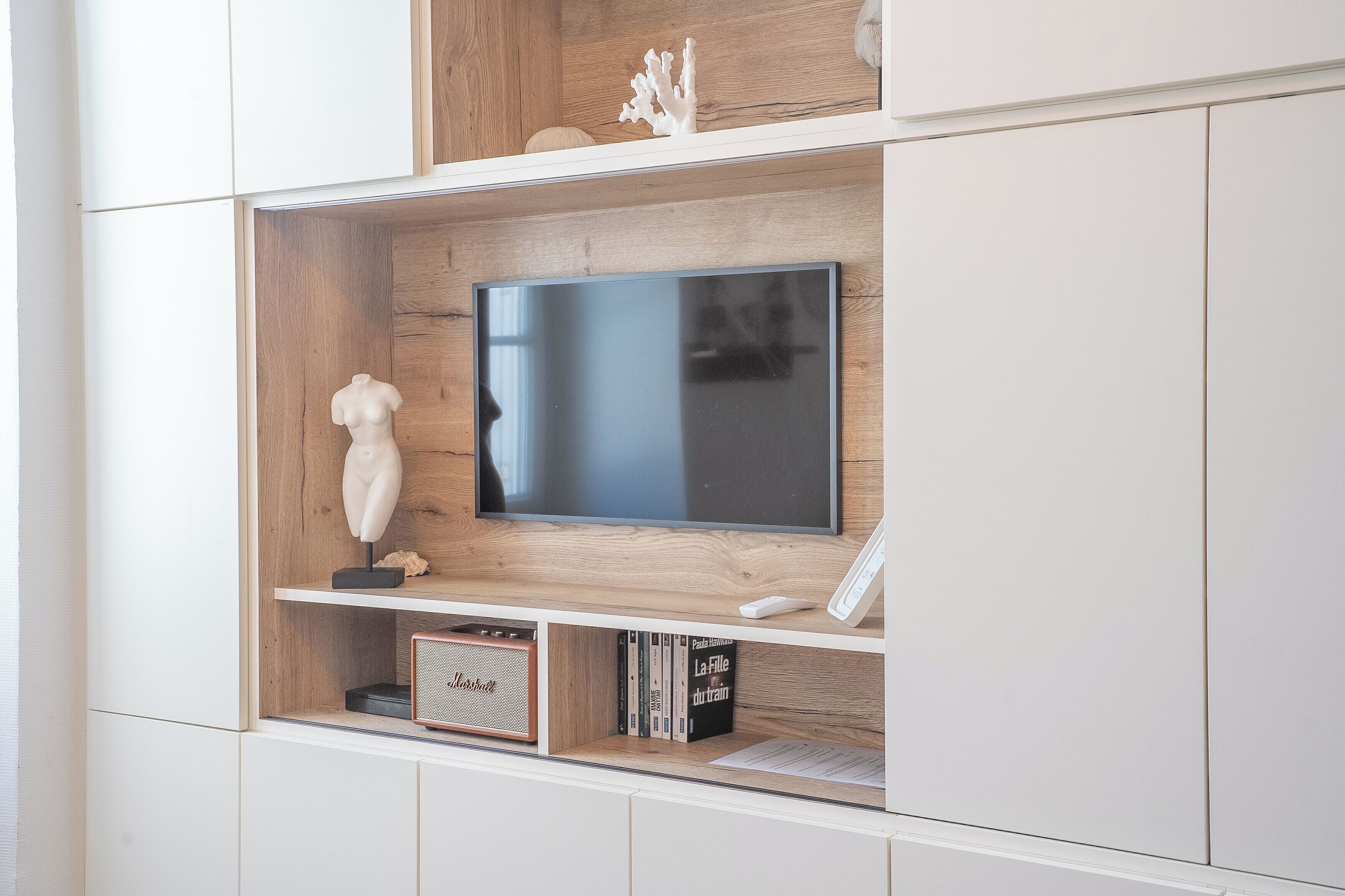 A modern entertainment unit with a flat-screen TV, a small sculpture, and a bookshelf with books and a speaker.