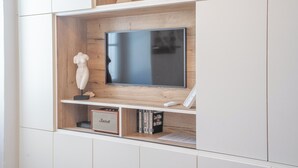 Et moderne tv-møbel med et fladskærms TV, en lille skulptur og en reol med bøger og en højttaler.