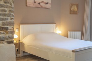 A neatly made bed in a room with a stone wall, a bedside table with a lamp, and a radiator. - La Rabine – Bel Appartement avec Terrasse Privée (Vannes)