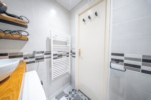 A bathroom with a white sink, a towel rack, a shower, and a door with a towel holder. - La Rabine – Bel Appartement avec Terrasse Privée (Vannes)