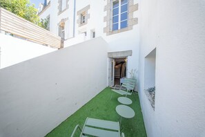 A narrow courtyard with artificial grass, a bench, and a table. - La Rabine – Bel Appartement avec Terrasse Privée (Vannes)