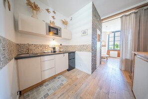A modern kitchen with a microwave, sink, and cabinets, leading to a dining area with a view. - La Rabine – Bel Appartement avec Terrasse Privée (Vannes)