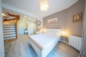 A bedroom with a large bed, a wooden staircase, a stone wall, and a ceiling light fixture. - La Rabine – Bel Appartement avec Terrasse Privée (Vannes)