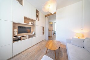 A modern living room with a flat-screen TV, wooden flooring, and a sofa. - La Rabine – Bel Appartement avec Terrasse Privée (Vannes)