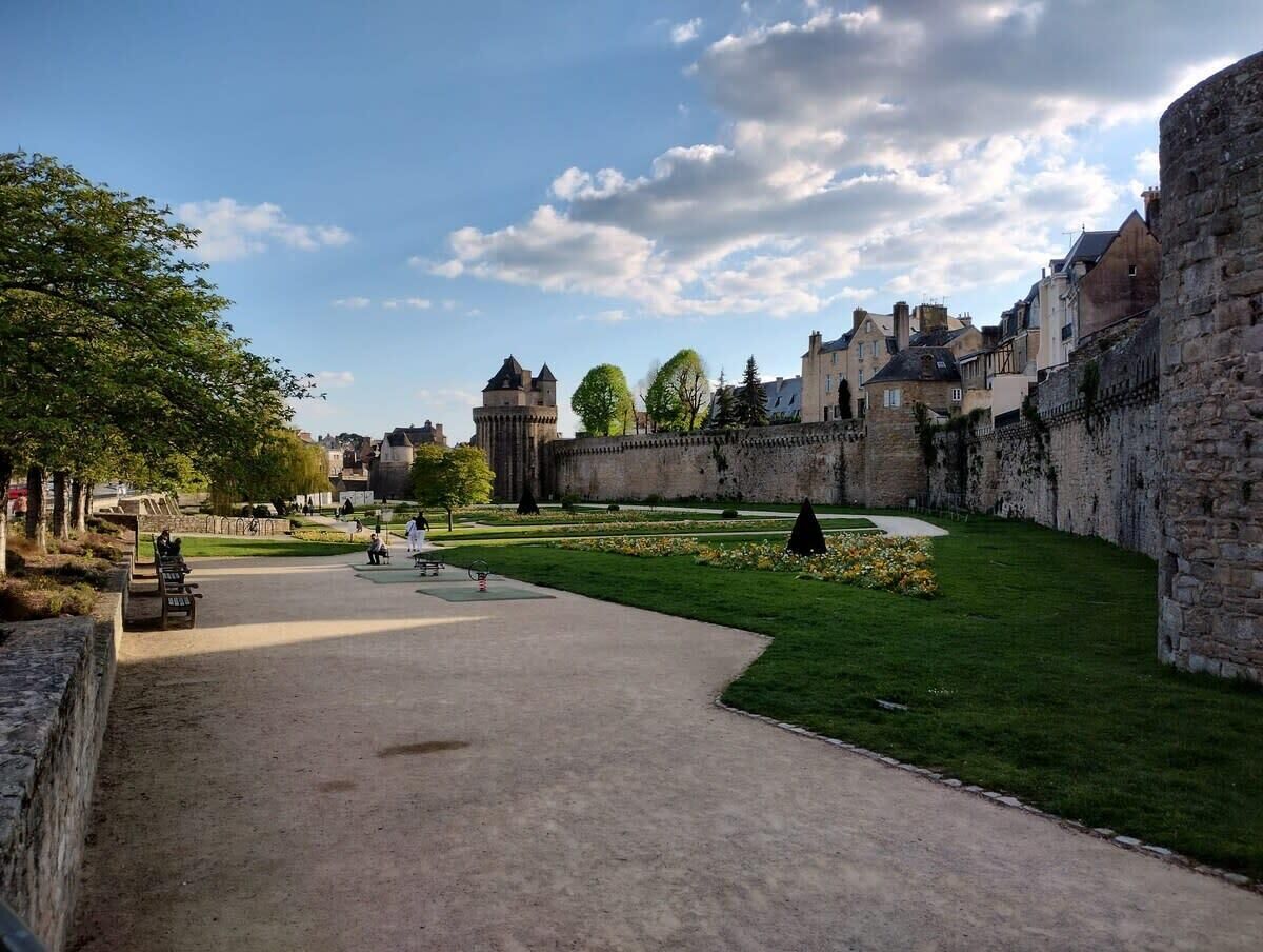 A historical courtyard with stone walls, a paved walkway, and a grassy area with flowers.