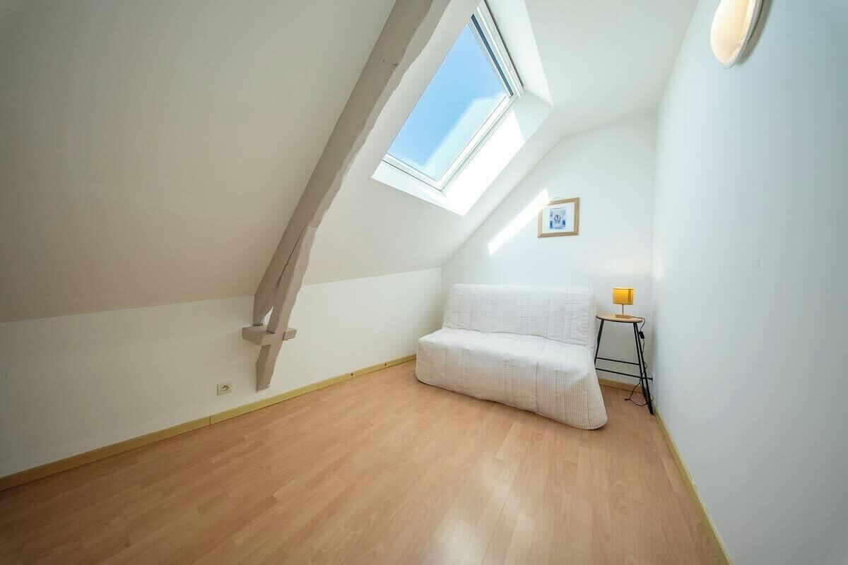 A room with a sloped ceiling, a skylight, a white sofa, and a small table with a lamp.