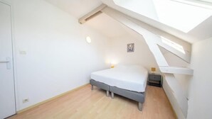 Un dormitorio con tragaluz, cama, mesita de noche y mesilla.