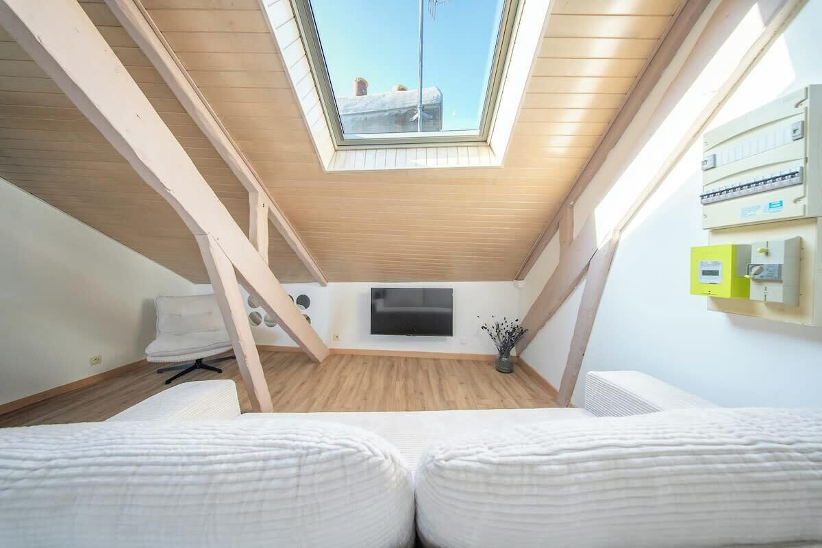 A room with a sloped ceiling, a skylight, a flat-screen TV, and a bed with white bedding.