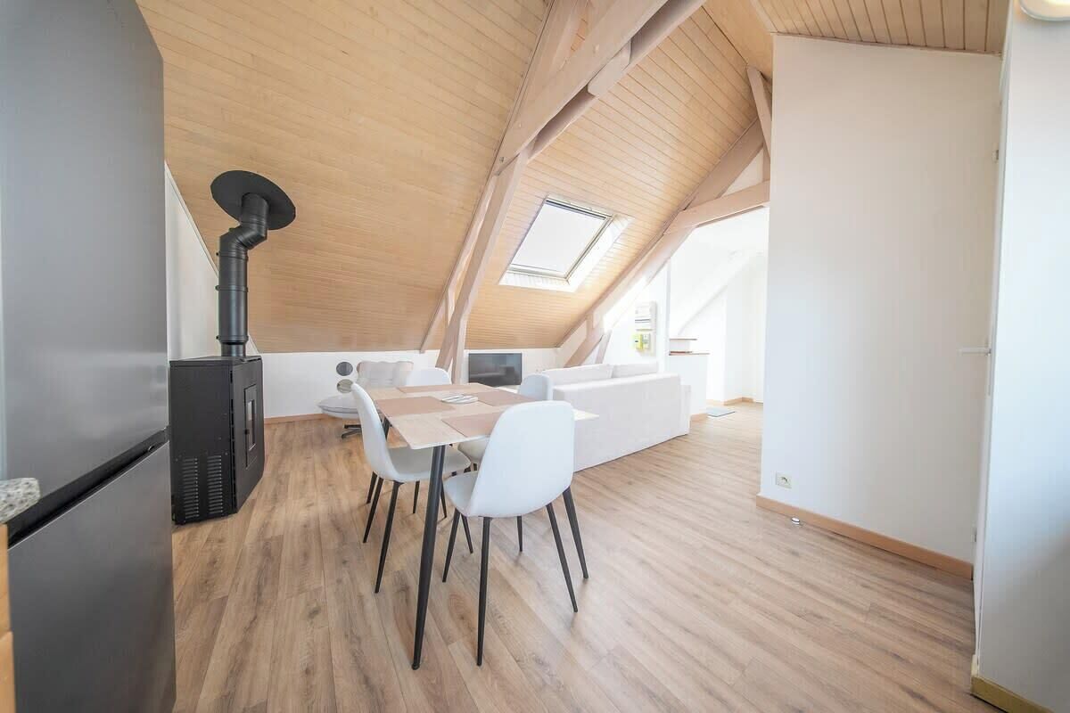 Un dormitorio tipo loft moderno con techo inclinado, chimenea empotrada, sofá blanco y comedor con mesa y sillas.