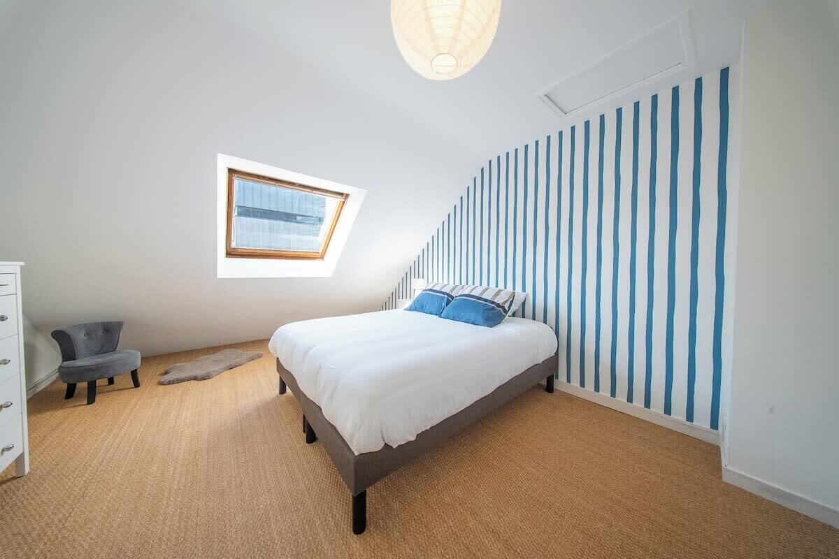Un dormitorio con cama, una silla, cómoda, ventana y papel tapiz a rayas.