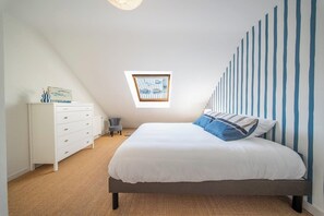 Une chambre à coucher avec un lit, une commode, une fenêtre et un plafond en pente.
