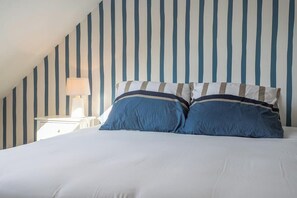 Un dormitorio con cama, almohadas, una mesita de noche y una lámpara.