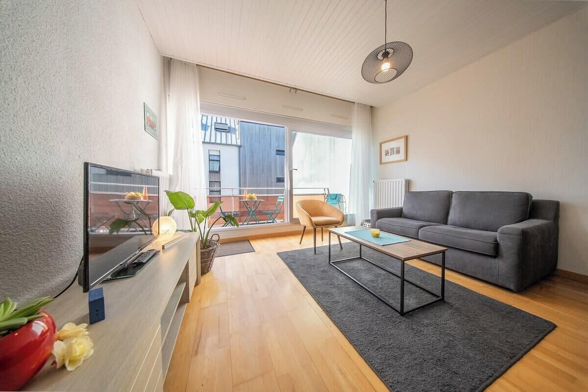 Un soggiorno moderno con un divano, un tavolino da caffè e una televisione. C'è un balcone con vista sugli edifici.