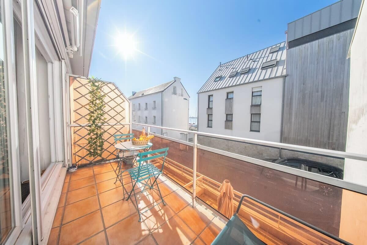 A balcony with a table and chairs, a potted plant, and a view of neighboring buildings.