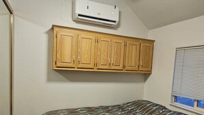 A bedroom with a bed, wooden cabinets, an air conditioner, and a ceiling fan. - Peaceful 1.5-bedroom Tiny home with AC/Heat in Winnemucca with beautiful sunsets (Winnemucca)