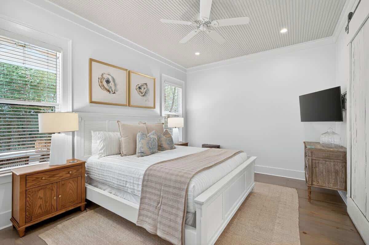 Ein Schlafzimmer mit Bett, Nachttischen, Deckenventilator, Fernseher und Wandbild.