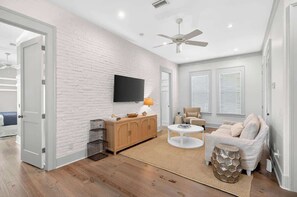 Ein modernes Wohnzimmer mit weißer Ziegelwand, Deckenventilator, Flachbildfernseher, Holzschrank, beiges Sofa und rundem Couchtisch.