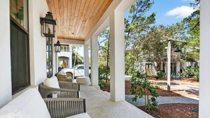 A covered outdoor seating area with wicker furniture and a view of a residential property. - Luxe Beach House: Steps to Rosemary, Beach, Pool & Bikes (Inlet Beach)
