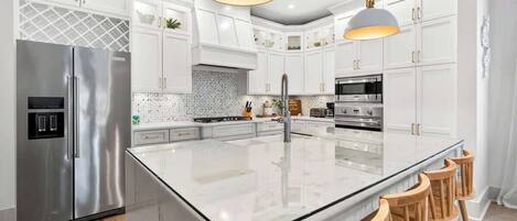 A modern kitchen with white cabinetry, stainless steel appliances, a large island with bar stools, and pendant lighting.