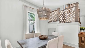A dining area with a rectangular table, white chairs, a hanging light fixture, and a decorative wall panel. - Luxe Beach House: Steps to Rosemary, Beach, Pool & Bikes (Inlet Beach)