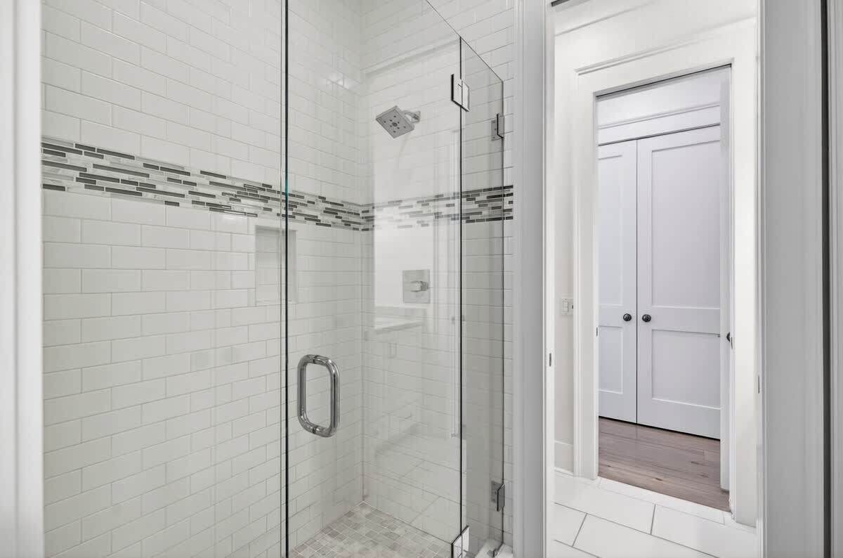 A modern bathroom with white subway tiles, a glass shower enclosure, and a white door.