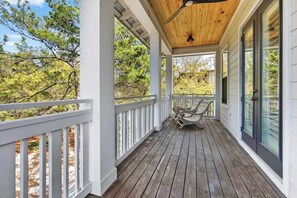 Une véranda couverte avec un plancher en bois, des balustrades blanches et un ventilateur de plafond.