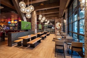 Ein Restaurant mit Holztischen, Bänken, hängenden Kugelleuchten und großen Fenstern.