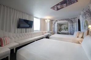 A hotel room with a sofa, two beds, a TV, and a chandelier.