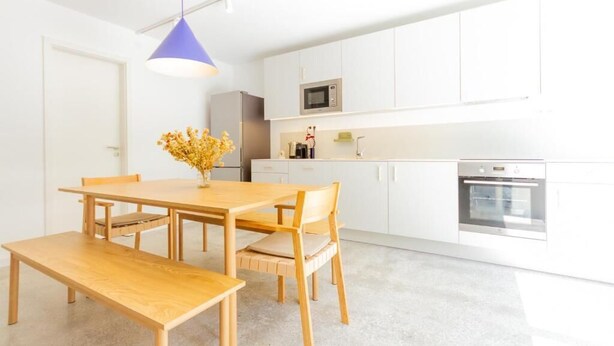 Une cuisine moderne avec des meubles blancs, un four à micro-ondes, un four traditionnel et un coin repas comprenant une table et des chaises en bois.