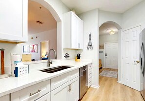 A modern kitchen with white cabinetry, a stainless steel sink, and a decorative Eiffel Tower wall art. - Coconico Retreat At Windsor Palms (Kissimmee)