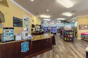 A reception area with a counter, a clock, a vending machine, and a sign indicating sundry shop hours. - Coconico Retreat At Windsor Palms (Kissimmee)