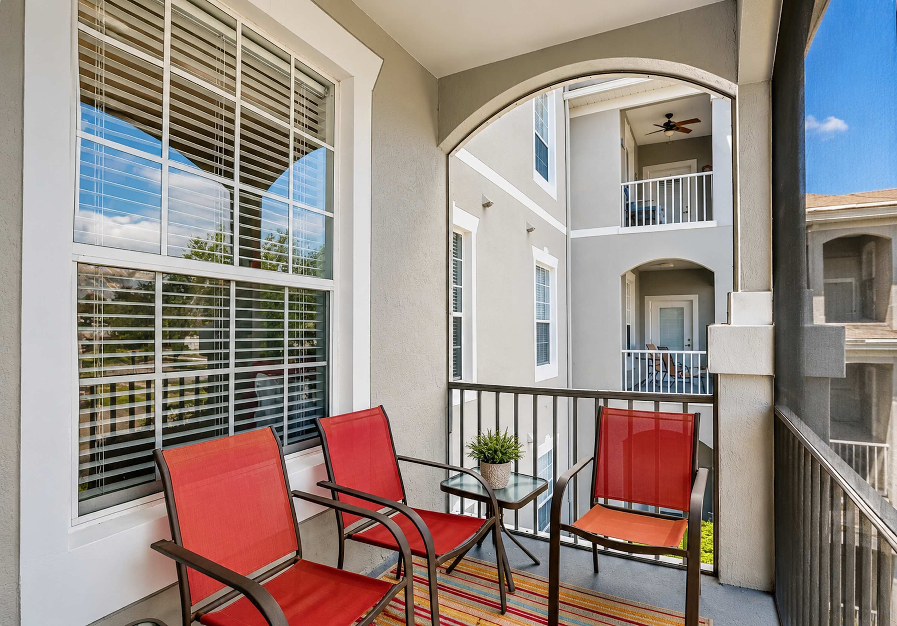 A balcony with two red chairs, a glass table, and a potted plant.
