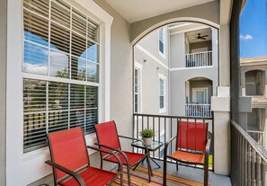 A balcony with two red chairs, a glass table, and a potted plant. - Coconico Retreat At Windsor Palms (Kissimmee)