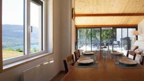 Un coin repas avec une table en bois dressée pour quatre personnes, de grandes fenêtres offrant une vue sur un paysage montagneux et une porte-fenêtre coulissante donnant sur une terrasse extérieure.
