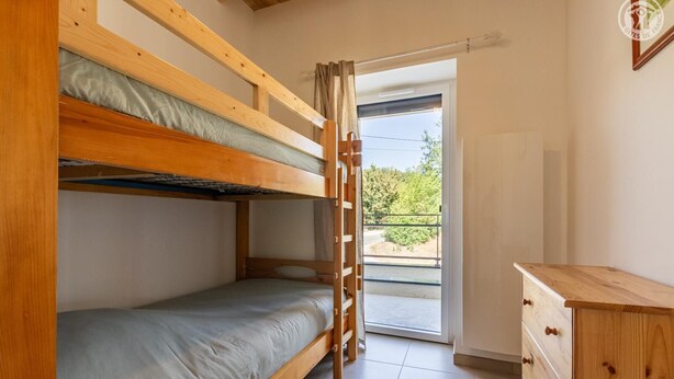 Une chambre avec deux lits superposés, une commode en bois et une porte-fenêtre coulissante donnant sur un espace extérieur.