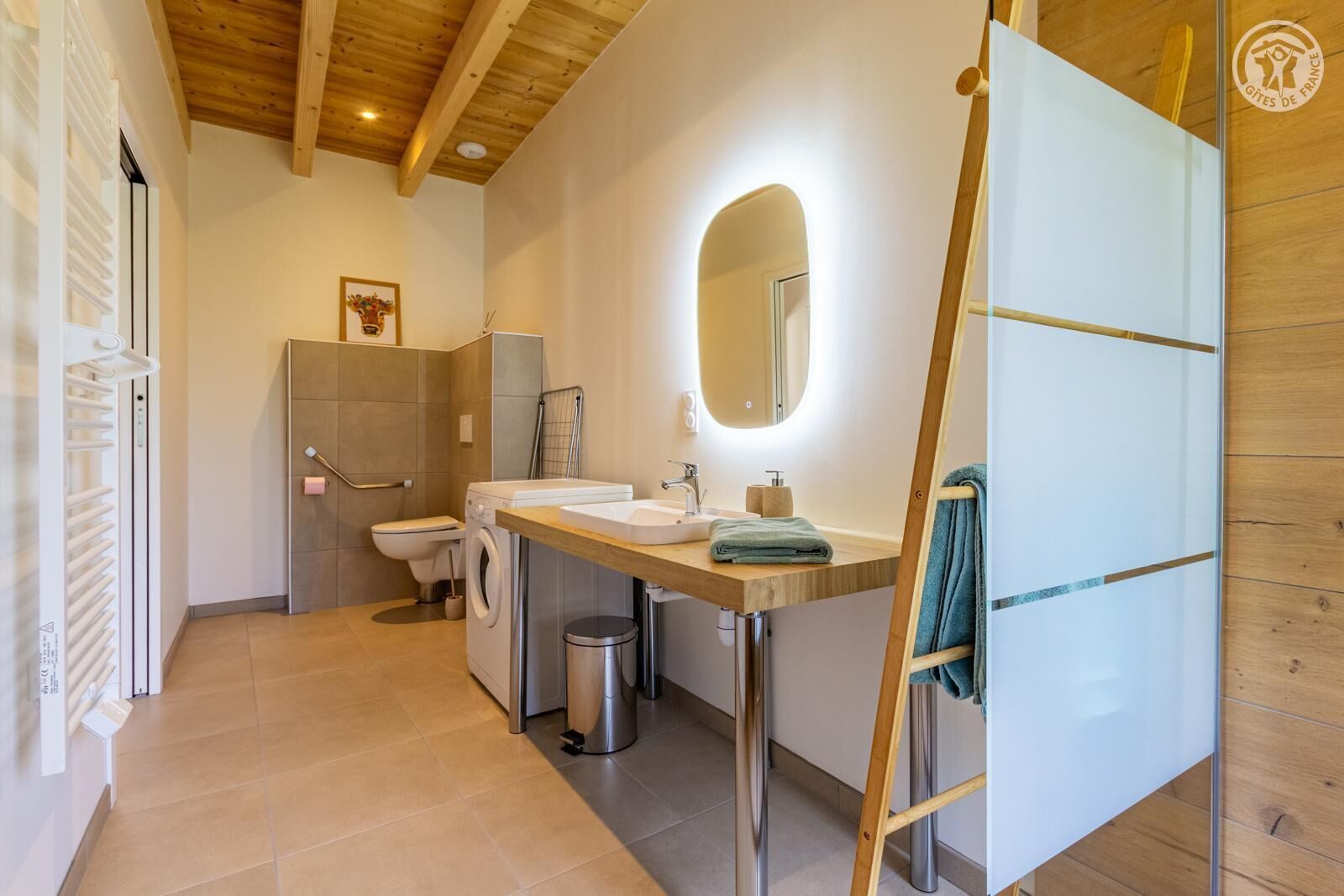 Une salle de bain moderne avec un plafond en bois, deux lavabos, des toilettes, un lave-linge et un miroir.
