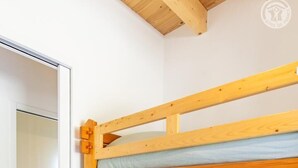 Un lit superposé avec une structure en bois et un matelas, une machine à laver en arrière-plan et un sol carrelé.