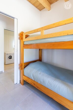 Ein Stockbett mit Holzrahmen und einer Matratze, eine Waschmaschine im Hintergrund und ein gefliestes Badezimmer.