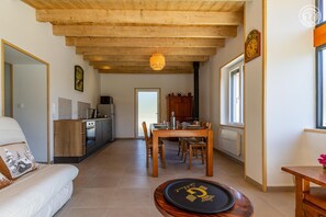 Un interior modern amb sostre de fusta, zona de menjador amb taula i cadires, cuina amb electrodomèstics i sofà amb coixí.