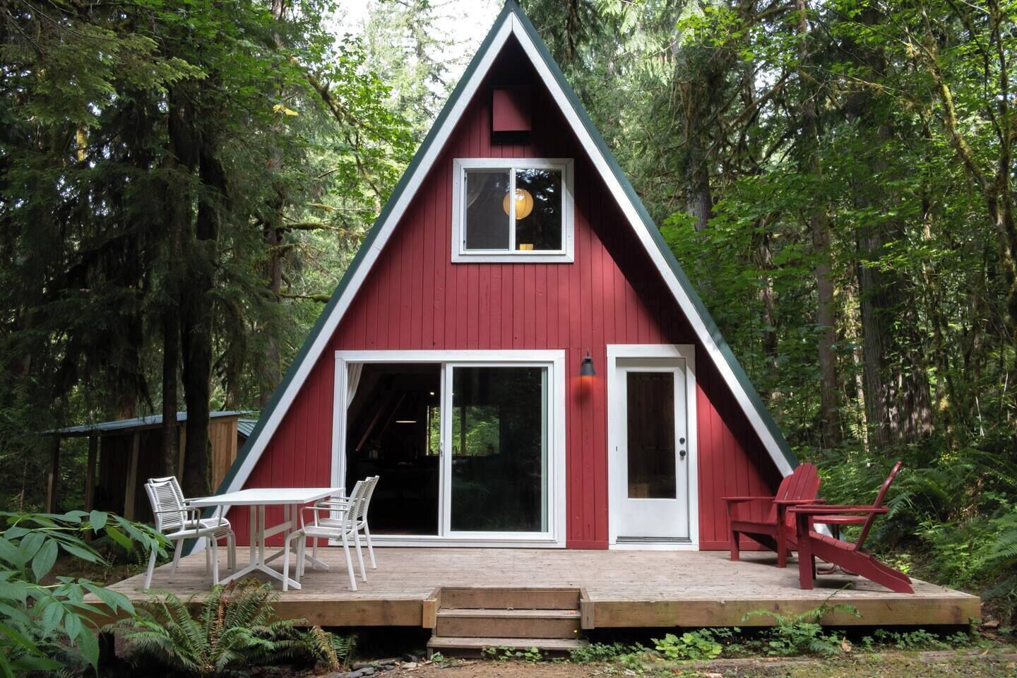 A red A-frame cabin with a sliding glass door, a small deck, and outdoor seating.