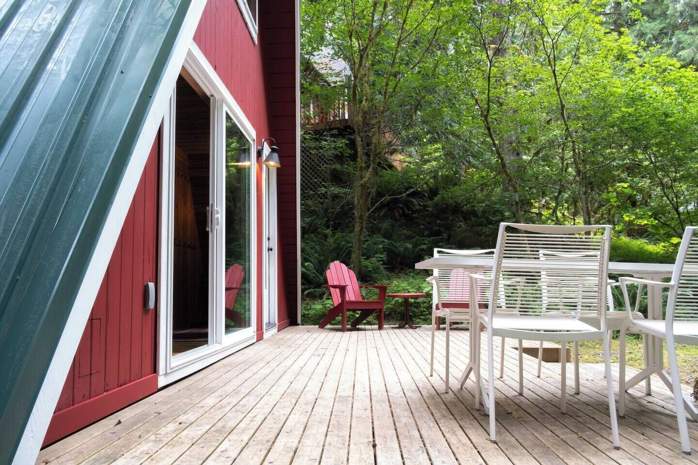 Une terrasse en bois avec des sièges d’extérieur, un bâtiment rouge doté d’une porte-fenêtre coulissante et un toit végétalisé.