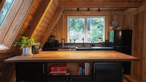 A kitchen with a wooden countertop, a sink, a stove, and a window. There are three stools and a shelf with books. - Forest A-Frame & Sauna : Dog Friendly + Pool (Deming)