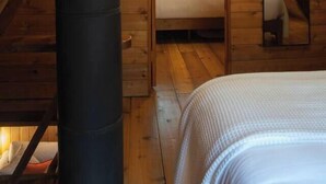 A wooden cabin interior with a bed, a visible chimney, and a window with curtains. - Forest A-Frame & Sauna : Dog Friendly + Pool (Deming)