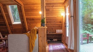 A cozy cabin interior with a loft bed, a small table with a plant, a bench outside, and a view of the forest through the window. - Forest A-Frame & Sauna : Dog Friendly + Pool (Deming)
