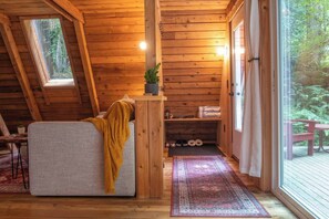 A cozy cabin interior with a loft bed, a small table with a plant, a bench outside, and a view of the forest through the window. - Forest A-Frame & Sauna : Dog Friendly + Pool (Deming)